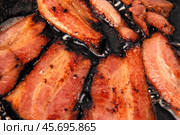 Frying Bacon Slices in a Pan. Crispy Pieces of Delicious Red Thin Smokey Bacon Fried in a Hot Skillet. Traditional Breakfast. Smoked Bacon Rasher or Strip Being Cooked. Grill. Fat High Calorie Food. Стоковое фото, фотограф Марина Демидюк / Фотобанк Лори