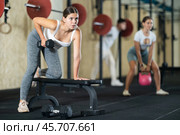 Athletic young woman pumping her biceps with a dumbbell while leaning on bench. Стоковое фото, фотограф Яков Филимонов / Фотобанк Лори