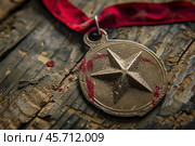 Old tarnished medal with red ribbon resting on wooden surface. Стоковое AI-изображение, AI-художник Иван Рябоконь / Фотобанк Лори