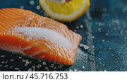Salmon Fillet. Fresh salmon fillet with parsley and lemon slices. Sliced raw pink salmon fish steak with cooking ingredients, herbs on a wooden cutting board on a dark black background, top view. Стоковое AI-видео, аниматор Марина Демидюк / Фотобанк Лори