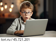 A young Caucasian male worker in glasses looks unhappy while sitting at a desk with a laptop during a workday in a dimly lit office. Стоковое AI-изображение, AI-художник Sergey Grishin / Фотобанк Лори