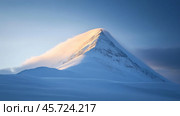 Snow-capped mountain peak glows in the sunlight with dramatic clouds surrounding the summit at dusk. Стоковое AI-изображение, AI-художник Сергей Толмачёв / Фотобанк Лори