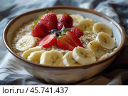 Bowl of oatmeal topped with banana slices, fresh strawberries, blueberries, and a sprinkle of oats, served in a ceramic dish on a soft fabric background. Стоковое AI-изображение, AI-художник Башкирова Анна / Фотобанк Лори