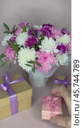 Vertical video of a woman's hand bringing holiday gifts in boxes to a beautiful bouquet of fresh flowers. Holiday greeting card for birthday, March 8, Valentine's Day, Mother's Day or family holiday. Стоковое видео, видеограф Виктория Катьянова / Фотобанк Лори