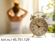Blurred Woman waking up and stretching her arm, focus on the alarm clock at 10 o'clock in the morning. Closeup vintage retro style alarm clock, young Asian girl wake up sitting on bed. Hello, new day. Стоковое AI-изображение, AI-художник Марина Демидюк / Фотобанк Лори