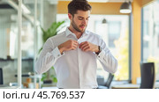 Elegant businessman buttoning shirt in modern office, getting ready for work. Стоковое AI-изображение, AI-художник Юрий Поздников / Фотобанк Лори