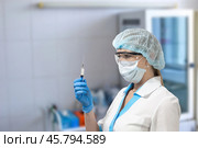 A nurse in a mask and glasses holds a syringe and looks at it, preparing an injection for a patient, Стоковое фото, фотограф Коханова Наталья / Фотобанк Лори
