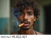 A young man residing in Cuba smokes a cigar while looking directly at the viewer, showcasing a unique hairstyle and a calm demeanor in a vibrant environment. Generative AI. Стоковое AI-изображение, AI-художник Юлия Петровская / Фотобанк Лори