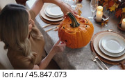 Woman is carving a pumpkin on a table with a tablecloth and plates. Стоковое AI-видео, аниматор Sergey Grishin / Фотобанк Лори