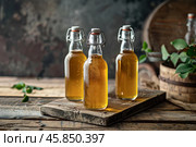 Three bottles of fresh kombucha resting on rustic wood. Стоковое AI-изображение, AI-художник Иван Рябоконь / Фотобанк Лори