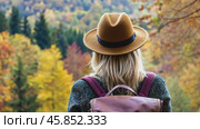 Adventurer among an Autumn Landscape. Back View of Young Woman Wearing Knitted Hat, Jacket, Backpack in Forest Woods Nature. Beauty and Adventure. Vibrant colorful fall scenery. Travel hike. Journey. Стоковое AI-видео, аниматор Марина Демидюк / Фотобанк Лори