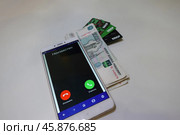 Входящий, неизвестный номер на смартфоне, деньги и банковские карточки на белом фоне. Incoming unknown number on the smartphone, money and bank cards on a white background. (2024 год). Редакционное фото, фотограф Юрий Пуликов / Фотобанк Лори