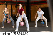 Girl in gym does exercises with kettlebell, lifts and lowers heavy kettlebell with one hand. Стоковое фото, фотограф Яков Филимонов / Фотобанк Лори