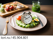 Intermittent fasting showing vegetables and alarm clock on plate. Стоковое AI-изображение, AI-художник Иван Рябоконь / Фотобанк Лори