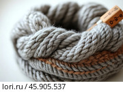 A close-up of a skein of thick gray yarn is shown. The knitting is made of soft and fluffy wool, with thick weaves visible, making it ideal for creating cozy items such as sweaters, scarves, or blankets. A contrasting brown stripe runs down the center of the skein, adding an accent. On the right is a wooden tag or label with numbers printed on it, which may indicate the length or composition of the yarn. The background is blurred, drawing attention exclusively to the texture and details of the knitting. Стоковое AI-изображение, AI-художник Анна Кривицкая / Фотобанк Лори