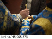 Priest in blue church vestment anoints with sacred oil from golden vessel. Стоковое фото, фотограф irisff / Фотобанк Лори