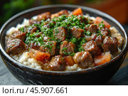 A delicious and filling hot dish in a deep bowl. The base of the dish is white rice, which acts as a side dish. On top of the rice are juicy pieces of fried meat, browned to a golden brown crust. Between the meat you can see pieces of carrot and, possibly, onion, soaked in a rich sauce. Finally, the dish is generously sprinkled with finely chopped fresh green onions, which add freshness and brightness to the taste. The dishes are made of dark ceramics, which adds contrast and enhances the aesthetic appeal of the dish. The composition creates a cozy feeling of home or restaurant food. Стоковое AI-изображение, AI-художник Анна Кривицкая / Фотобанк Лори