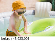 It's a hot day. A cute boy in sunglasses and a panama hat swims on a circle in a foam pool. The concept of summer holidays with children. Стоковое фото, фотограф Photojuli / Фотобанк Лори