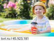 It's a hot summer day. Cute boy swims in the pool. The child drinks refreshing lemonade. The concept of summer holidays with children and refreshing drinks. Стоковое фото, фотограф Photojuli / Фотобанк Лори