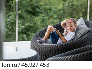 A 5-year-old little boy with a smartphone in his hands on the veranda. The child is playing on the phone. Harm of gadgets for children. Protect your child from the smartphone. Kids and gadgets. Стоковое фото, фотограф Photojuli / Фотобанк Лори