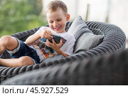 A 5-year-old little boy with a smartphone in his hands on the veranda. The child is playing on the phone. Harm of gadgets for children. Protect your child from the smartphone. Kids and gadgets. Стоковое фото, фотограф Photojuli / Фотобанк Лори