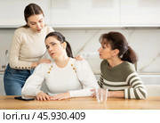 Sad woman sits silently in kitchen, adult girls sympathize and comfort her. Стоковое фото, фотограф Яков Филимонов / Фотобанк Лори