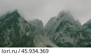 A cloudy mountain range with steep cliffs and lush greenery at the base. Стоковое видео, видеограф Igor Tichonow / Фотобанк Лори