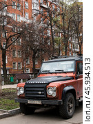 Легковой автомобиль повышенной проходимости Land Rover Defender припаркован на обочине дороги во дворе красного кирпичного дома на ул. Куусинена в Москве (2024 год). Редакционное фото, фотограф Алиса Сокол / Фотобанк Лори