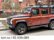 Автомобиль Land Rover Defender припаркован на обочине дороги во дворе красного кирпичного дома на ул. Куусинена в Москве весной в апреле (2024 год). Редакционное фото, фотограф Алиса Сокол / Фотобанк Лори
