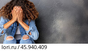 A woman sits near a concrete wall, covering her face with her hands, conveying feelings of distress, sadness, and anxiety. Copy space. Стоковое AI-изображение, AI-художник Михаил Строгалев / Фотобанк Лори