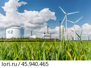 Hydrogen storage tanks marked with H2 and wind turbines stand in a green, eco-friendly landscape, under a bright sky. Стоковое AI-изображение, AI-художник Михаил Строгалев / Фотобанк Лори