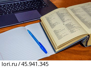 Школьная тетрадь в линейку, большой орфографический словарь русского языка, ручка и ноутбук лежат на столе. Концепция изучения русского языка и ограничения использования заимствованных слов. Стоковое фото, фотограф Владимир Устенко / Фотобанк Лори