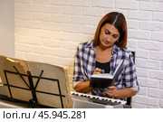Beautiful woman in checkered shirt playing music synthesizer at home, composes music, learns musical scores. Стоковое фото, фотограф Ольга Яковенко / Фотобанк Лори