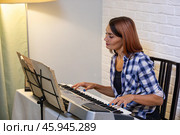 Beautiful woman in checkered shirt playing music synthesizer at home, composes music, learns musical scores. Стоковое фото, фотограф Ольга Яковенко / Фотобанк Лори