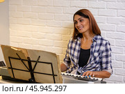 Beautiful woman in checkered shirt playing music synthesizer at home, composes music, learns musical scores. Стоковое фото, фотограф Ольга Яковенко / Фотобанк Лори