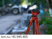 A construction site with a geodetic instrument (optical level) on a tripod in the foreground. Construction equipment in the blurred background. Стоковое фото, фотограф Роман Дзюбало / Фотобанк Лори