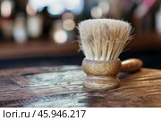 Shaving brush with natural bristles is standing on wooden table in barbershop. Стоковое AI-изображение, AI-художник Иван Рябоконь / Фотобанк Лори