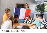 Joyful female teacher discussing with preteens students state flag of France in auditory of middle school. Стоковое фото, фотограф Яков Филимонов / Фотобанк Лори