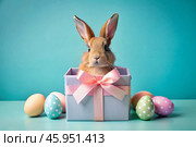 A holiday banner. A cute Easter bunny is peeking out of a gift box, and colorful eggs are scattered around. The concept of happy Easter. Стоковое AI-изображение, AI-художник Photojuli / Фотобанк Лори