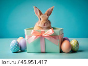 A holiday banner. A cute Easter bunny is peeking out of a gift box, and colorful eggs are scattered around. The concept of happy Easter. Стоковое AI-изображение, AI-художник Photojuli / Фотобанк Лори