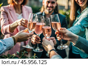 Glasses of pink sparkling wine in the hands of people. People are relaxing on the outdoor veranda. The concept of recreation, corporate event, party or celebration. Стоковое AI-изображение, AI-художник Photojuli / Фотобанк Лори