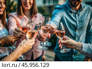 Glasses of pink sparkling wine in the hands of people. People are relaxing on the outdoor veranda. The concept of recreation, corporate event, party or celebration. Стоковое AI-изображение, AI-художник Photojuli / Фотобанк Лори
