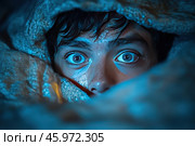 A close-up of the person's face is shown surrounded by fabric, creating a framing effect. The main focus is on the bright blue, wide-open eyes, which express surprise or fear. The skin on the face is slightly damp, possibly due to sweat or light, which adds drama and tension. The light blue lighting enhances the effect of anxiety and emphasizes the contrast between the eyes, fabric and skin. The texture of the fabric around the face appears soft and rough, creating a cozy, yet tense context. The composition of the photograph conveys an atmosphere of intrigue, emotional tension and mystery. Стоковое AI-изображение, AI-художник Анна Кривицкая / Фотобанк Лори