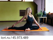 Blonde middle-aged woman doing Eka Pada Rajakapotasana, pigeon pose variation, practicing in black sportswear, sitting on colorful mat in yoga studio. Стоковое фото, фотограф Сергей Чайко / Фотобанк Лори