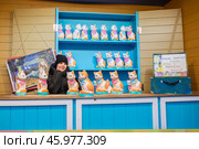 Россия, Москва, Площадь Революции - Январь 2025. Девочка за прилавком с кошками - копилками на рынке. Декорации из фильма Леонида Гайдая "Операция "Ы" и другие приключения Шурика. Фотозона. Russia, Moscow, Revolution Square - January 2025. The girl behind the counter with the piggy bank cats at the market. Scenery from Leonid Gaidai's film "Operation Y" and other adventures of Shurik. The photo zone. Стоковое фото, фотограф Мария / Фотобанк Лори