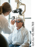 Ophthalmologist examining patient's eyesight with a phoropter in clinic. Стоковое AI-изображение, AI-художник Юрий Поздников / Фотобанк Лори