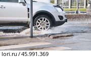 Silver sedan splashing water while driving through urban street puddle, wet asphalt reflecting vehicle's dynamic motion. Стоковое фото, фотограф Mikhail Davidovich / Фотобанк Лори