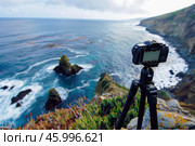 Camera on tripod capturing breathtaking ocean view from clifftop. Стоковое AI-изображение, AI-художник Иван Рябоконь / Фотобанк Лори