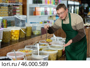 Seller man in supermarket showing and scooping marinated green olives. Стоковое фото, фотограф Яков Филимонов / Фотобанк Лори