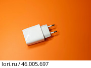 Блок питания USB без кабеля на оранжевом фоне, вид сверху. Адаптер питания, зарядное устройство для бытовой электроники. Редакционное фото, фотограф Sergei Gorin / Фотобанк Лори